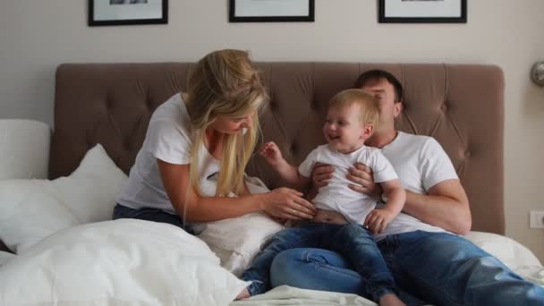 Los padres cariñosos juegan con su hijo en la cama riendo y sonriendo en el dormitorio — Vídeo de stock