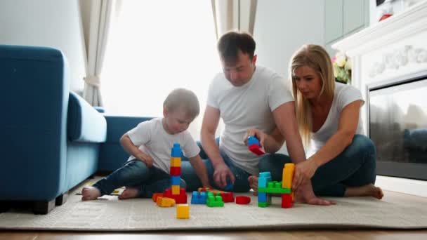 Щаслива родина тато мама і дитина 2 роки грають в лего у своїй світлій вітальні. Стрілянина повільного руху щаслива сім'я — стокове відео