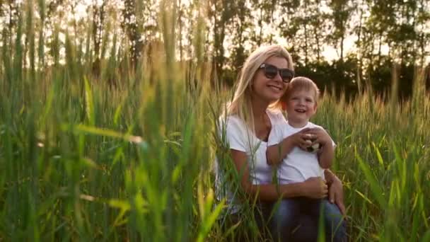Amante mãe e filho abraçando e brincando com uma bola de futebol em um campo com espiguetas em bela luz do pôr do sol em camisetas brancas — Vídeo de Stock