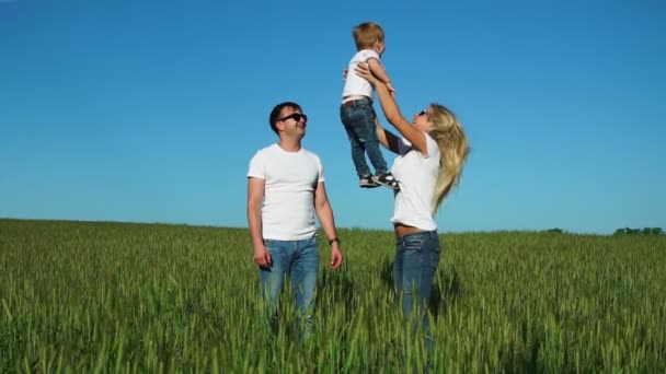 Familia feliz: Padre madre e hijo saltan y ríen en el campo vistiendo camisetas blancas y jeans — Vídeos de Stock