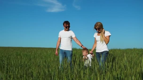 Mutter, Vater und Sohn gehen mit Spikes in weißen T-Shirts und Jeans auf das Feld und lächeln sich fröhlich an — Stockvideo