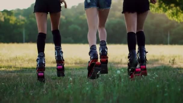 Три девушки в сапогах с пружинами бегают по летнему парку на закате занимаясь спортом — стоковое видео