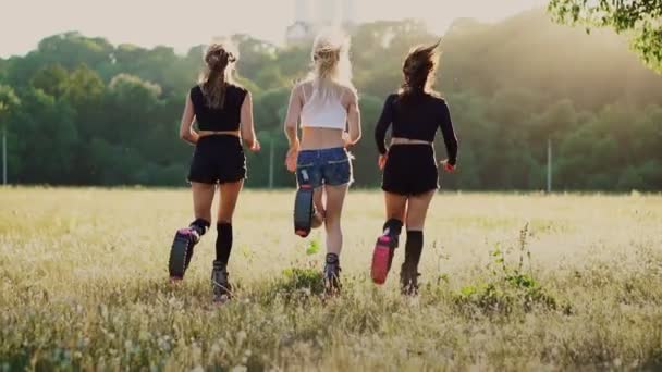 Три девушки в сапогах с пружинами бегают по летнему парку на закате занимаясь спортом — стоковое видео