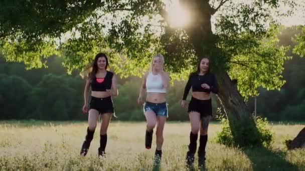 Trois filles en bottes avec des ressorts traversant le parc d'été au coucher du soleil faisant du sport — Video