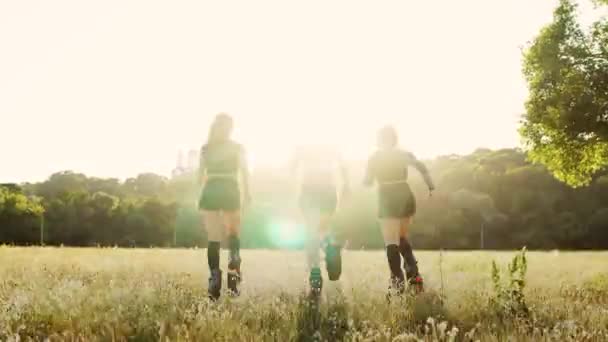 Три дівчини в чоботях з пружинами проходять через літній парк на заході сонця займаються спортом — стокове відео