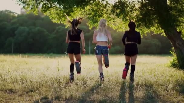 Três meninas de botas com molas correndo pelo parque de verão ao pôr do sol fazendo esportes — Vídeo de Stock