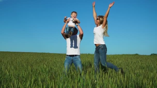 Familia feliz: Padre madre e hijo saltan y ríen en el campo vistiendo camisetas blancas y jeans — Vídeos de Stock