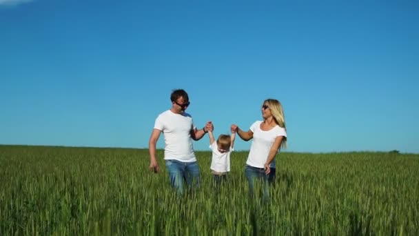 母父と息子は、彼の手にそれを振る白い t シャツとジーンズの楽しみのスパイク フィールドで歩く — ストック動画