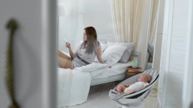 Anne cep telefonu görünüyor ve sosyal ağlar ve beyaz bir iç bebek çürük sandalyede yanındaki yazdığı.