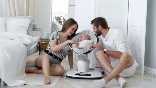 Nahaufnahme glücklicher Eltern, die ihrem kleinen Baby beim Schlafen in einem Schaukelstuhl für Babys zu Hause in einer weißen Wohnung zusehen — Stockvideo