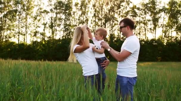 Молодые родители идут на поле с шипами пшеницы в белых футболках и джинсах — стоковое видео