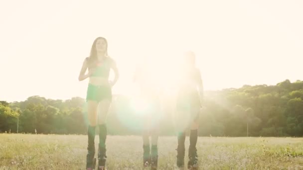 Drei Mädchen in Stiefeln mit Federn, die bei Sonnenuntergang durch den Sommerpark laufen und Sport treiben — Stockvideo