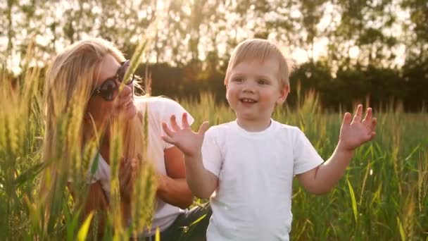 El concepto de una familia feliz. Primer plano de un niño y su madre en un campo con espigas de trigo sonriendo y jugando con una pelota de fútbol — Vídeos de Stock