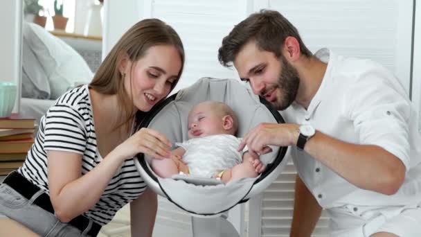 Close - up of happy parents watching their little baby sleep in a rocking chair for babies — Stock Video