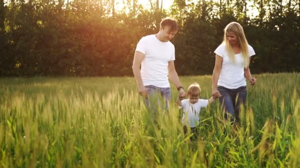 Мать отец и сын гуляют по полю с шипами в белых футболках и джинсах весело размахивая ими на руках — стоковое видео