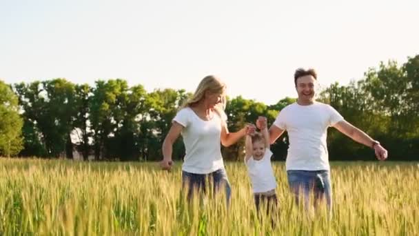 Família feliz: Pai, mãe e filho, correndo no campo vestidos com camisetas brancas — Vídeo de Stock