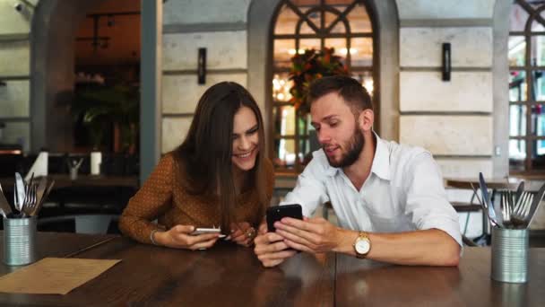 Найкращі друзі-жінки і чоловіки дивляться смішне відео на мобільний телефон, відпочивають разом у відкритому кафе, п'ють коктейль, перебуваючи у високій коктейлі. Веселі туристи переглядають фотографії на стільниковому зв'язку, з'єднані з Інтернетом — стокове відео