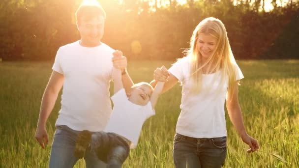 Mãe pai e filho caminham no campo com picos em camisetas brancas e jeans divertidos balançando nas mãos — Vídeo de Stock