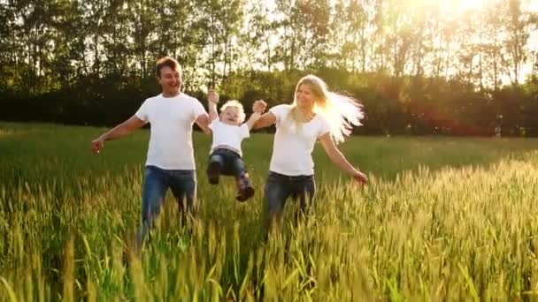 Mutter, Vater und Sohn laufen mit Spikes in weißen T-Shirts und Jeans über das Feld und schwingen es auf den Händen. — Stockvideo