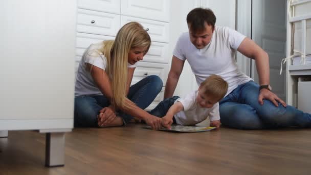 Een gezin van drie in witte T-shirts en blue jeans zittend op de vloer van hun slaapkamer spelen met de jongen in intellectuele spellen. Slow-motion-video schieten gelukkige familie — Stockvideo