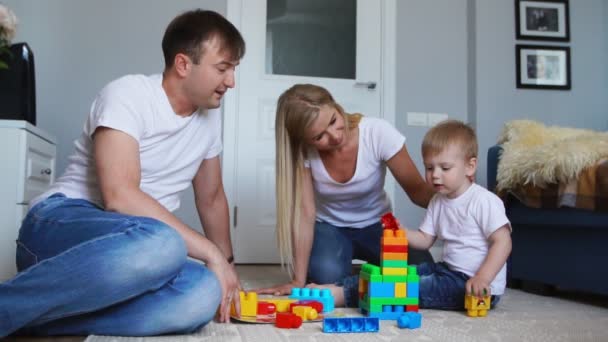 Gelukkig gezin vader moeder en baby 2 jaar lego spelen in hun lichte woonkamer. Slow-motion-video schieten gelukkige familie — Stockvideo