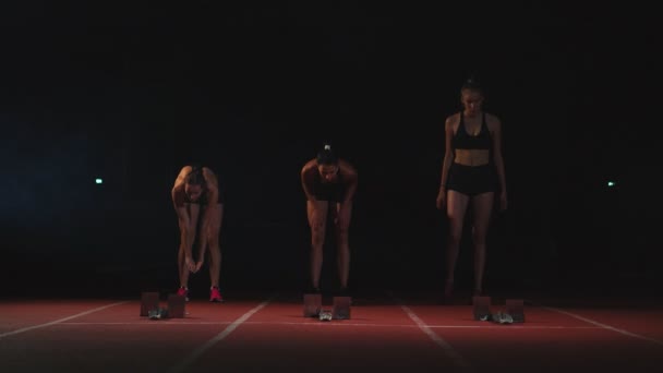 Три девушки спортсменки на старте готовятся к гонке и стартуют на беговой дорожке . — стоковое видео