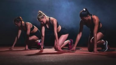 Üç spor kız sporcunun gece koşu bandı üzerinde siyah giysili oturma konumu sprint mesafede yarış için başlar.