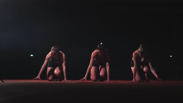 Tres chicas vestidas de negro están en las almohadillas de salida para comenzar la carrera en la competencia a la luz de las linternas . — Vídeo de stock