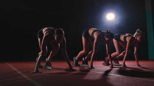 Vrouwelijke lopers op atletiek bijhouden gehurkt op de startblokken voor een race. In slow motion. — Stockvideo