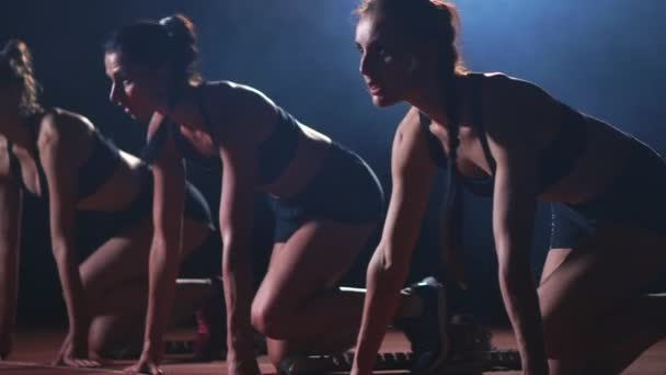 Drie meisjes in zwarte kleding zijn in de startende pads aan de start van de race in de competitie in het licht van de lichten en lopen naar de finish — Stockvideo