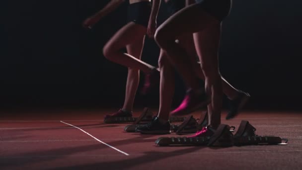 Três meninas em roupas pretas estão nas almofadas iniciais para iniciar a corrida na competição à luz das luzes e correr para o final — Vídeo de Stock