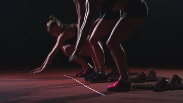 Três meninas em roupas pretas estão nas almofadas iniciais para iniciar a corrida na competição à luz das luzes e correr para o final — Vídeo de Stock
