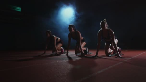 Vrouwelijke lopers op atletiek bijhouden gehurkt op de startblokken voor een race. In slow motion. — Stockvideo