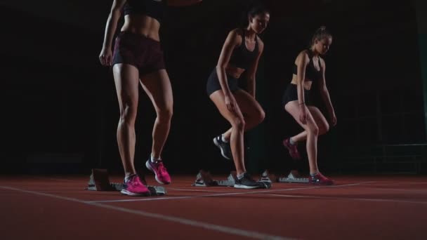 Corredores do sexo feminino no atletismo rastreiam agachamento nos blocos iniciais antes de uma corrida. Em câmara lenta . — Vídeo de Stock