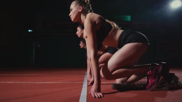 Женщины бегуны на легкой атлетике приседают на стартовых блоках перед гонкой. В замедленной съемке . — стоковое видео