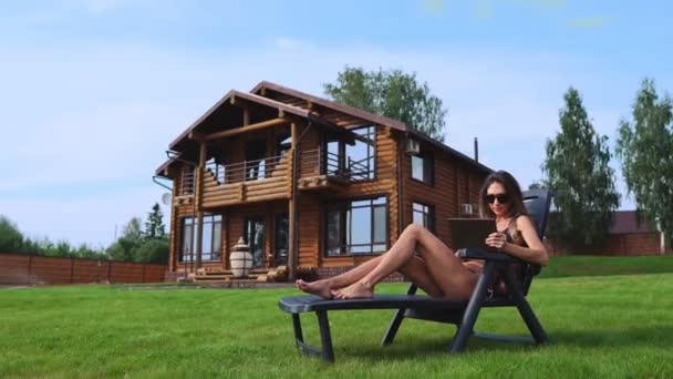 A beautiful sexy woman lying on a sun lounger in the backyard of her mansion is doing online shopping with a tablet computer — Stock Video
