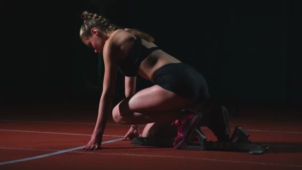Jonge vrouw atleet in zwarte korte broek en een t-shirt bereidt om te starten in de race voor 100 meter op de loopband in de buurt van de startlijn — Stockvideo