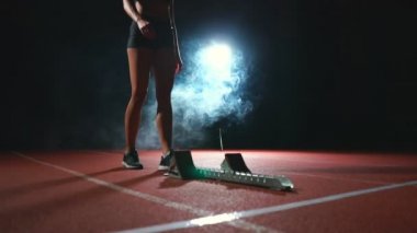Genç kadın atlet siyah şort ve tişört start çizgisinde yakınındaki koşu bandı üzerinde 100 metre yarışında başlatmak hazırlanıyor