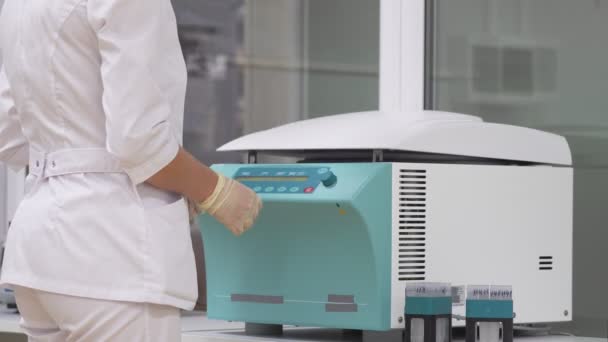 Au laboratoire, une femme en peignoir et gants met des échantillons de cellules humaines dans des éprouvettes dans une centrifugeuse pour dérouler et séparer les couches excédentaires de cellules. — Video