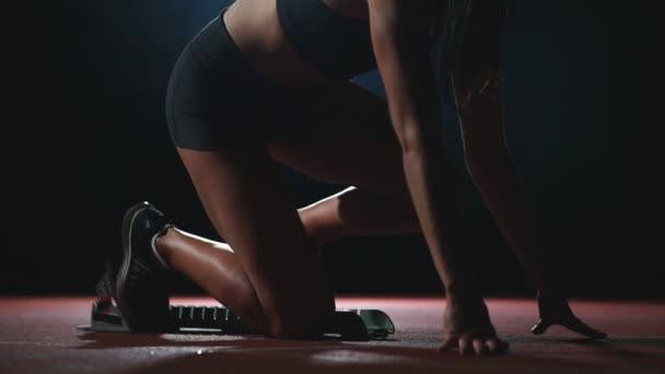 Стройная молодая девушка в легкой атлетике готовится к старту в гонке на беговых дорожках на черном фоне — стоковое видео