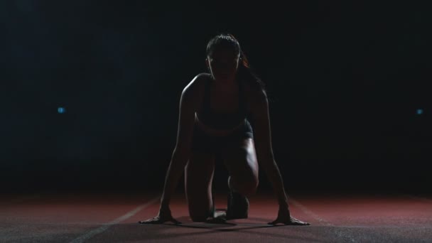 Jovem atleta em shorts pretos e uma camiseta está se preparando para começar a corrida por 100 metros na esteira perto da linha de início — Vídeo de Stock