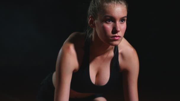 Professionele vrouw atleet op een donkere achtergrond gotovtes uit te voeren van de sprint van Jogging schoenen in sneakers op het spoor van het stadion op een donkere achtergrond. Close-up — Stockvideo