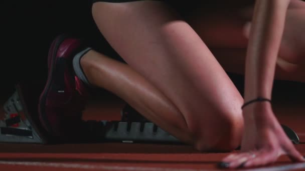 Γυναίκα επαγγελματίας αθλητής σε ένα σκοτεινό φόντο gotovtes για να εκτελέσετε την ορμή του Jogging παπούτσια σε πάνινα παπούτσια για το κομμάτι του γηπέδου σε σκούρο φόντο. Κοντινό πλάνο — Αρχείο Βίντεο