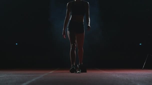 Mujer atleta profesional sobre un fondo oscuro para correr el sprint de los zapatos de correr en zapatillas de deporte en la pista del estadio sobre un fondo oscuro — Vídeos de Stock