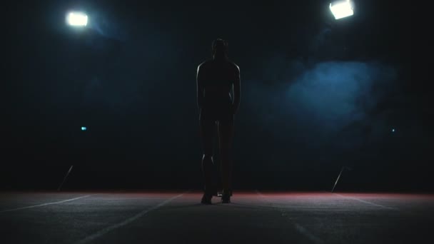 Athlète professionnelle sur fond sombre gotovtes pour courir le sprint de chaussures de jogging en baskets sur la piste du stade sur un fond sombre. Plan moyen — Video