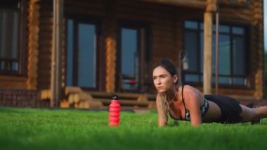 güzel esmer arka planda büyük bir köşkün fitness nişanlı ve açık havada eğitim basın için tahta egzersiz gerçekleştirir