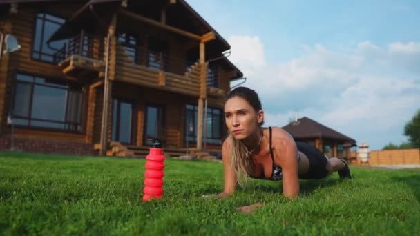Krásná brunetka na pozadí před velkým panským zabývající se fitness a provádí cvičení prkno pro tisk, trénink venku — Stock video