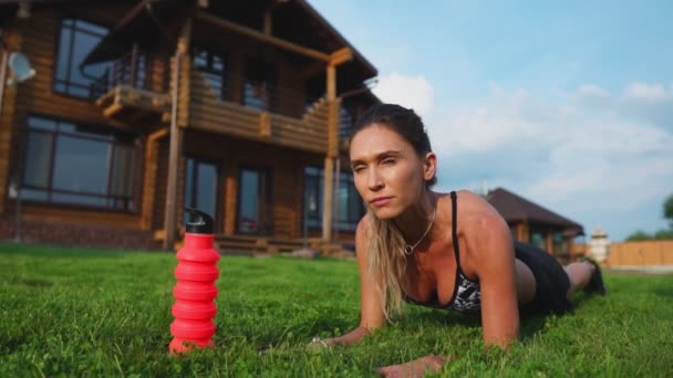 Mooie brunette op de achtergrond van een groot herenhuis bezig met fitness en presteert plank oefening voor de pers, opleiding buitenshuis — Stockvideo