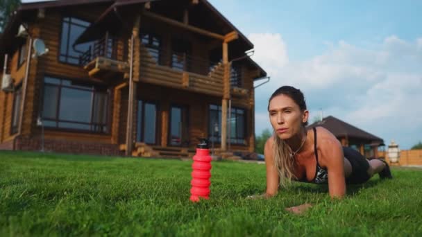 Hermosa morena en el fondo de una gran mansión dedicada a la aptitud y realiza ejercicio de tablón para la prensa — Vídeos de Stock