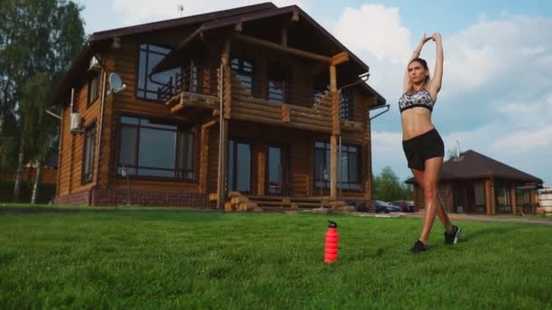 Mujer en el césped haciendo yoga en el fondo de una hermosa casa. El concepto de un estilo de vida saludable — Vídeo de stock